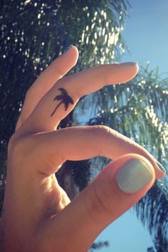 a person's hand with a small palm tree tattoo on their left index finger