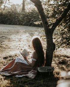 a woman sitting under a tree reading a book