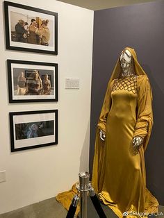 a yellow dress on display in front of some framed pictures and other art work at the museum