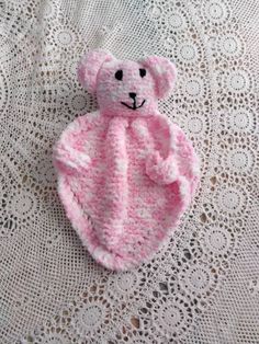 a crocheted pink teddy bear laying on top of a white doily covered table