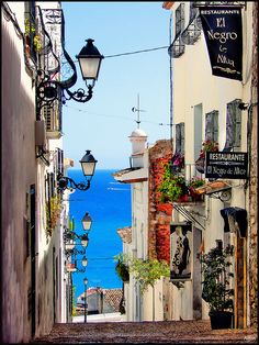 an alley way leading to the ocean with lots of lights hanging from it's sides