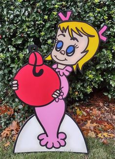 a wooden sign with a cartoon character holding a heart in front of some bushes and grass