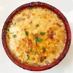 a baked dish with cheese and herbs in a red bowl on a white surface, top view