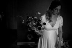 a woman in a white dress holding a bouquet of flowers and looking down at the floor