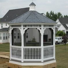 a white gazebo sitting on top of a lush green field next to a parking lot