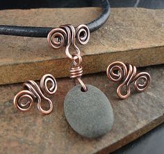 a wire wrapped necklace and earrings sitting on top of a rock next to a stone