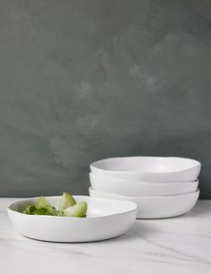 white bowls stacked on top of each other in front of a gray wall and marble countertop