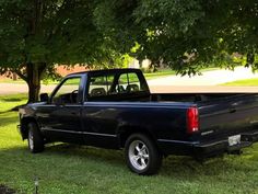 a black truck parked in the grass under a tree