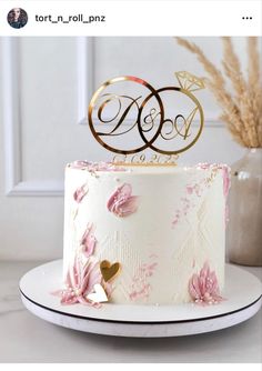 a wedding cake decorated with pink flowers and gold monogrammed topper is shown