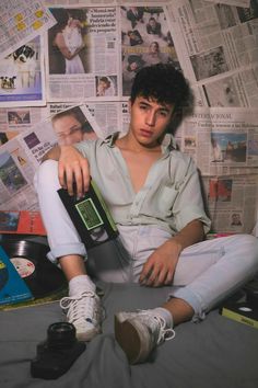 a young man sitting on top of a bed next to a wall covered in newspapers