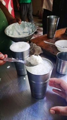 three cups filled with ice cream sitting on top of a metal table next to people