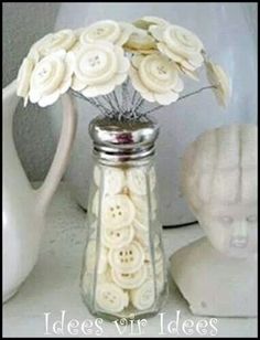 there is a vase with flowers in it and some buttons on the jar next to it