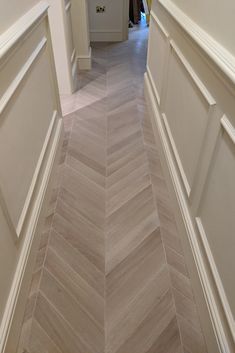 an empty hallway with white walls and wood flooring on either side, leading to another room