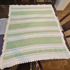 a green and white crocheted blanket sitting on top of a wooden chair next to a table