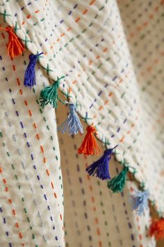 colorful tassels hang from the side of a white quilted bedding with orange, blue, and green trim