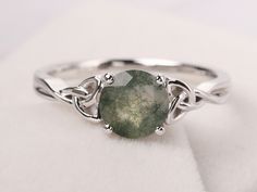 a close up of a ring with a green stone in it on a white surface