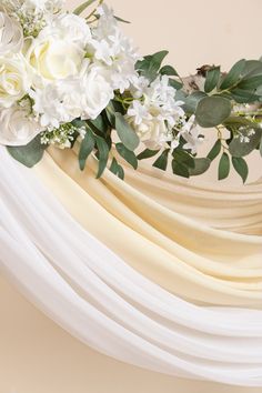 white flowers and greenery are arranged on top of the drape