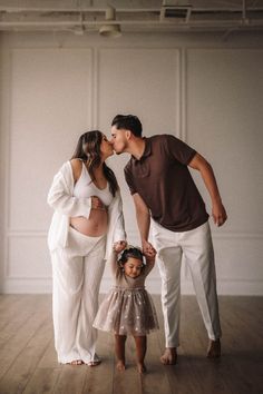 a pregnant woman and her husband kissing their daughter