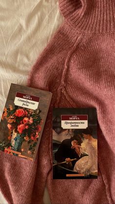 two books sitting on top of a bed next to an open pink sweater and white sheets