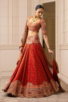 a woman in a red and gold lehenga is posing for the camera with her hand on her hip