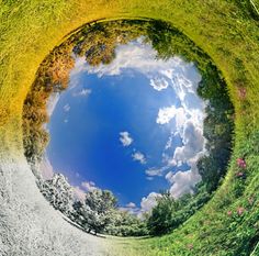 an image of the sky and clouds reflected in a round mirror with grass on both sides