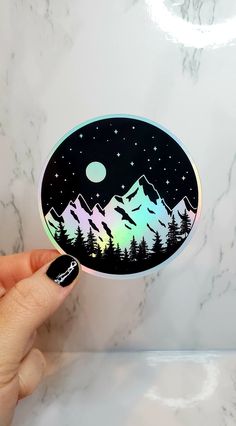 a person holding up a sticker with mountains and stars in the sky on it