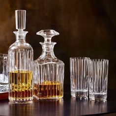 an assortment of liquor glasses and decanters on a table with one empty bottle