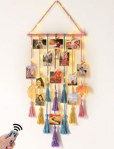 a person holding a remote control in front of a wall hanging with pictures and tassels