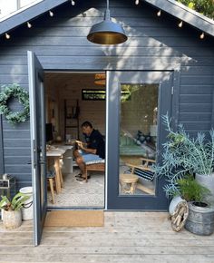 a man sitting at a table in the back of a blue shed with potted plants