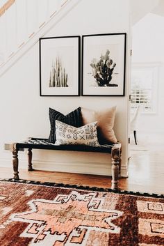 two paintings on the wall above a bench in a room with wooden floors and stairs