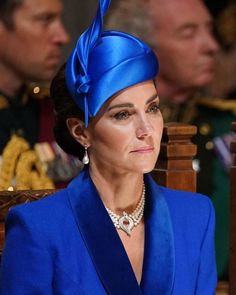 the queen is wearing a blue suit and hat with a large bow on her head