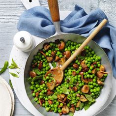 peas and mushrooms are being cooked in a pan with a wooden spoon on the side