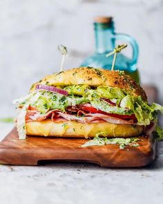 a sandwich with meat, lettuce and tomato on a cutting board next to a bottle