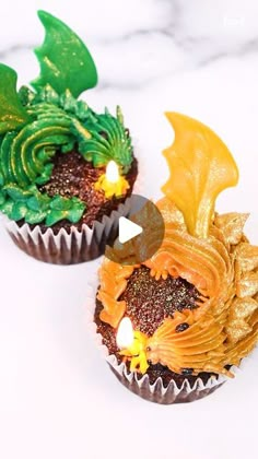 two cupcakes decorated with gold and green frosting are sitting on a marble surface