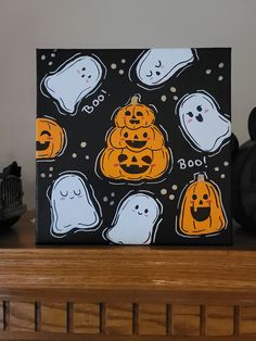 a halloween painting with ghost and pumpkins on black paper, sitting on a mantle