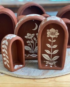 several clay planters with flower designs on them sitting on a wooden table next to each other