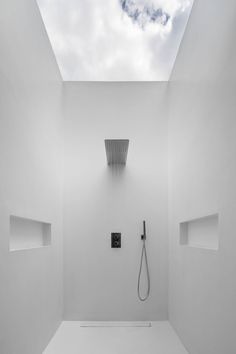 a white bathroom with skylight and shower head in the corner, on concrete floor