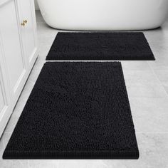 two black bath mats sitting on top of a bathroom floor next to a white tub