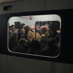 a group of people standing next to each other on a subway train, looking out the window