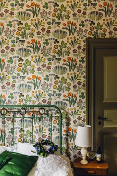 a bedroom with floral wallpaper and green bedding, along with a lamp on the nightstand