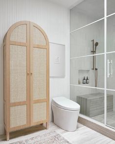 a white toilet sitting next to a wooden cabinet in a bathroom with glass doors on the wall