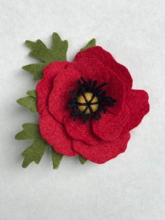 a red felt flower with green leaves on white background, closeup shot from above