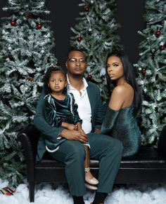 a man, woman and child sitting on a bench in front of a christmas tree