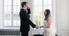 a bride and groom standing next to each other in front of a window holding hands