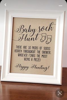 a baby sock hunt sign is displayed in a white frame on a wooden table next to a