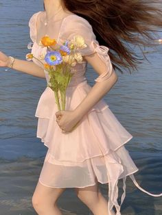 a woman in a pink dress holding flowers and walking into the water with long hair