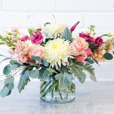 a glass vase filled with lots of flowers on top of a white countertop next to a brick wall