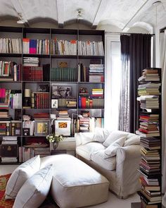 a living room filled with lots of books and furniture next to a tall book shelf