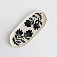 a black and white oval dish with leaves on the bottom, sitting on a white surface