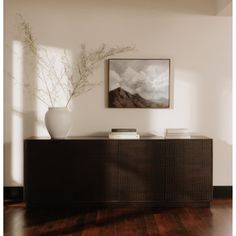 a vase sitting on top of a wooden table next to a wall with a painting above it